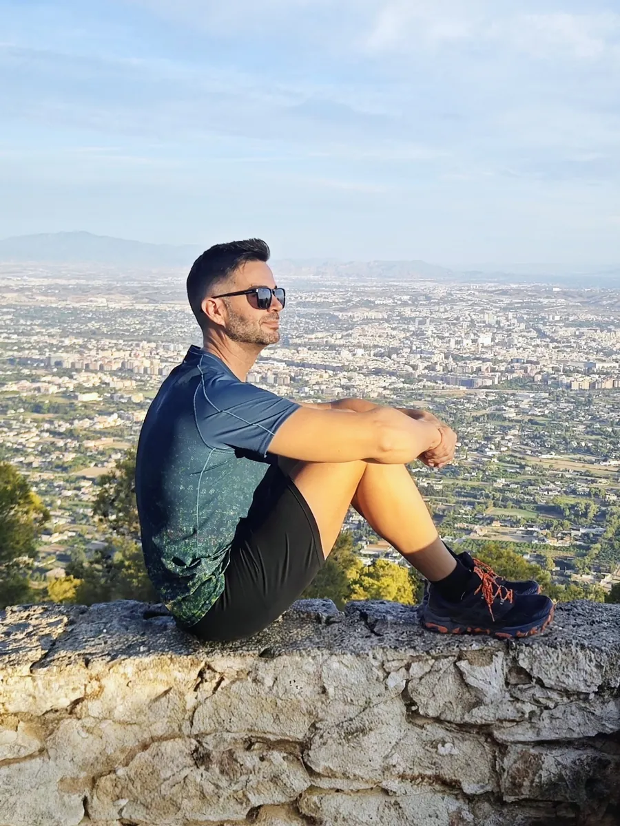 José, sentado en el muro de un mirador, mirando la ciudad al amanecer